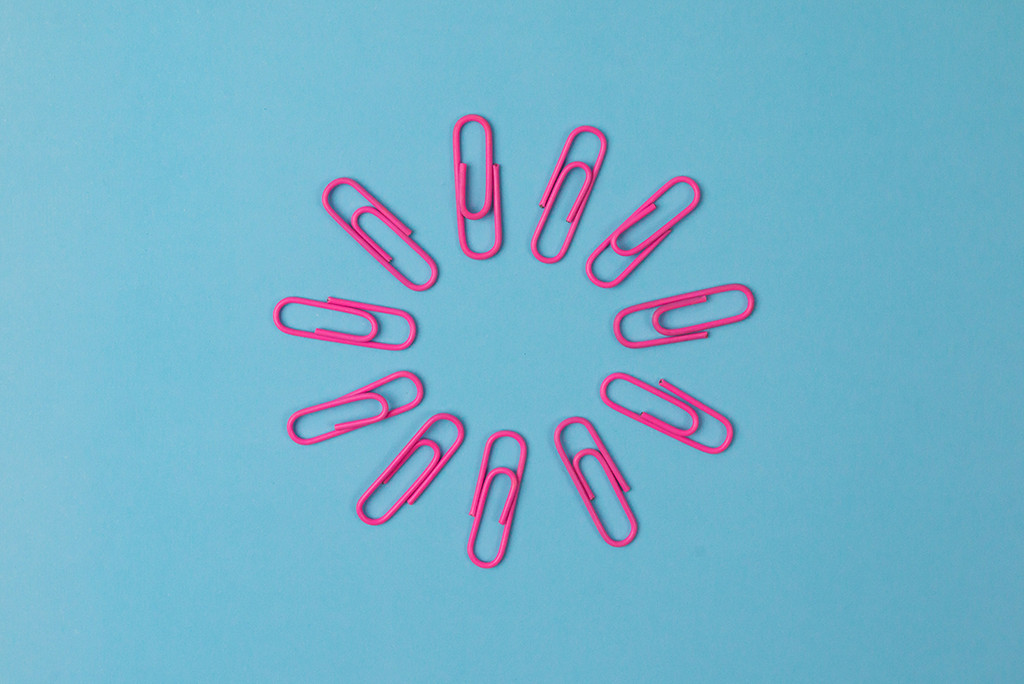Een cirkel van roze paperclips gelijkmatig gerangschikt op een blauwe achtergrond, die doet denken aan de nauwgezette organisatie die je ziet als je uitbesteden linkt.