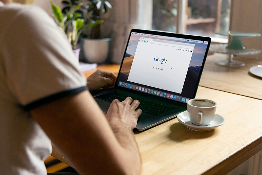 Een persoon die thuis een laptop gebruikt met Google open en onderzoek doet naar WordPress SEO. Op de houten tafel staan een potplant en een kopje koffie, wat bijdraagt aan de gezellige sfeer.